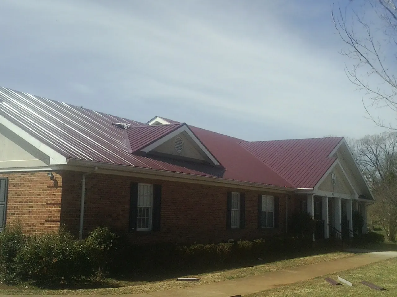 Red metal roof with gabled entries on a long brick building, from a Hail Damage Roof Repair job in Tennyson