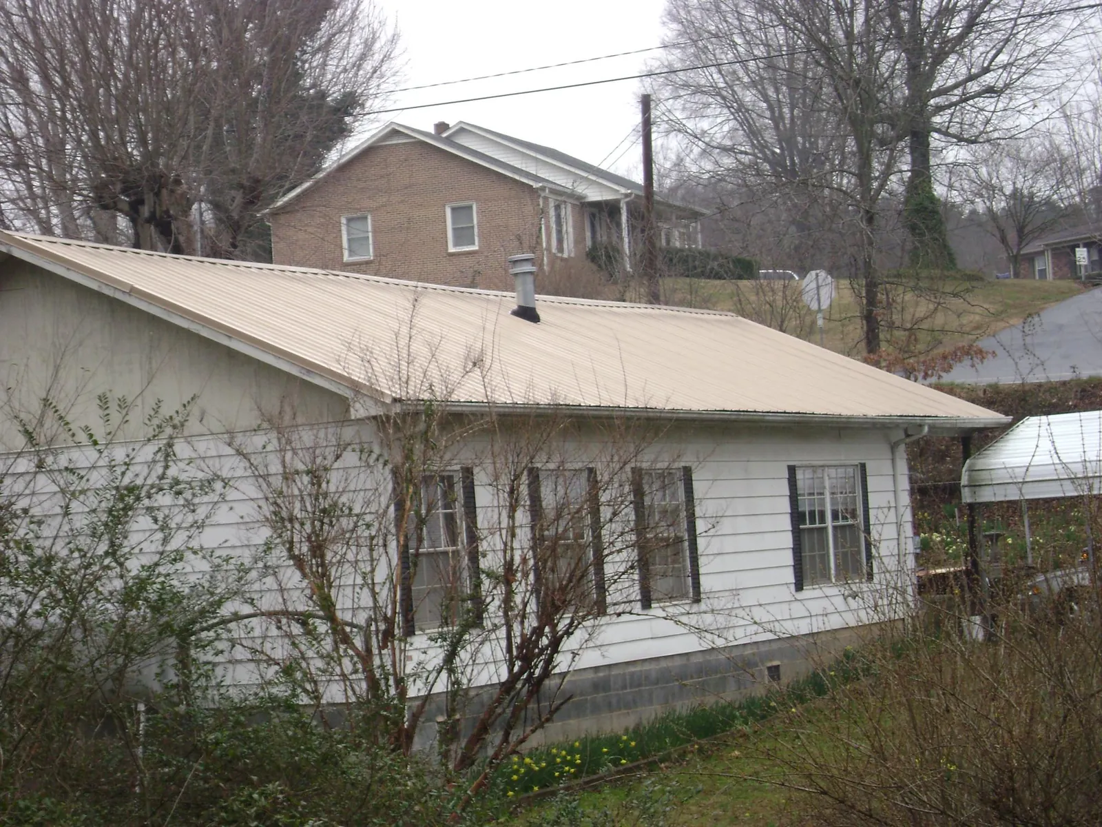Tan metal roof on a white sided house set into a hillside — Commercial Roofing by Roofing Brothers in Tennyson